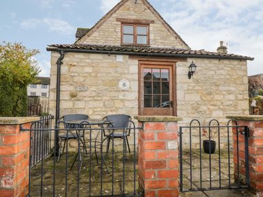 A stone cottage with a small patio area and outdoor table with two chairs at Chapel Cottage in Leonard Stanley near King's Stanley