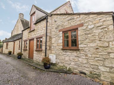 The exterior of a stone cottage with wooden windows and doors and potted plants on a gravel driveway at Chapel Cottage in Leonard Stanley near King's Stanley