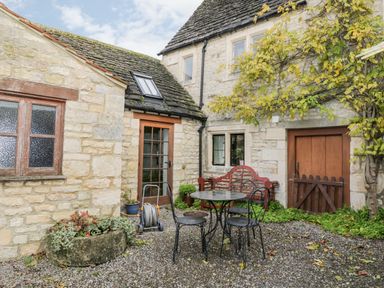A stone courtyard with outdoor table and chairs stone building with windows and wooden door at Chapel Cottage Leonard Stanley near Kings Stanley