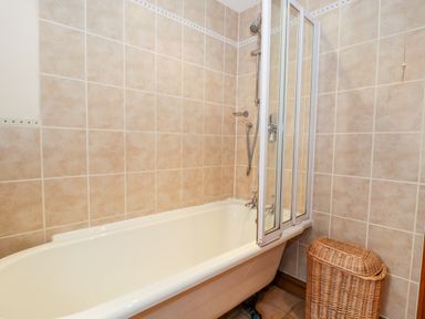 A bathroom with a bathtub shower enclosure and a wicker laundry basket at Chapel Cottage in Leonard Stanley near Kings Stanley