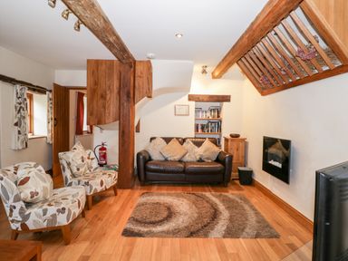 A living room with a leather sofa floral armchairs wooden beams and a wall-mounted fireplace at Chapel Cottage in Leonard Stanley near Kings Stanley