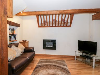 A living room with a leather sofa cushions a wall-mounted fireplace a TV on a glass stand and a bookshelf at Chapel Cottage Leonard Stanley near Kings Stanley