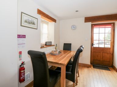 A dining area with a wooden table and four black chairs a wooden door and window at Chapel Cottage Leonard Stanley near Kings Stanley