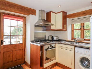 A kitchen with wooden door and window a gas stove oven kettle toaster sink and washing machine at Chapel Cottage in Leonard Stanley near Kings Stanley