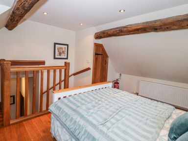 A bedroom with a bed near wooden stairs and exposed wooden beams at Chapel Cottage in Leonard Stanley near Kings Stanley