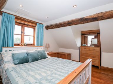 A bedroom with a wooden bed blue cushions and blue curtains a wooden dresser and a wooden beam ceiling at Chapel Cottage Leonard Stanley near Kings Stanley