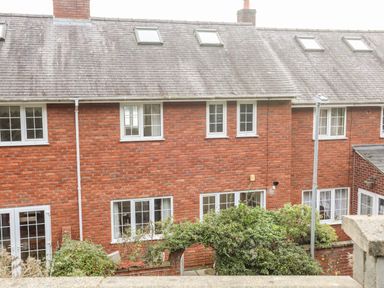 A brick terraced house with multiple windows and a sloped roof with skylights and a garden arch in front at Sea View Cottage in Menai Bridge