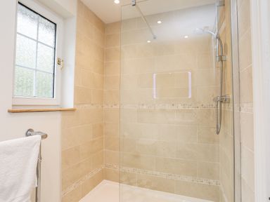 A bathroom with a walk in shower with beige tiles and a window at Sea View Cottage in Menai Bridge