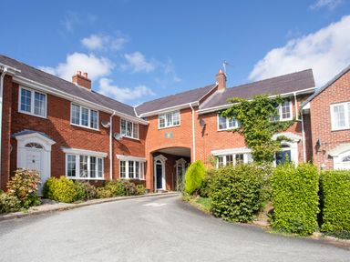 A row of red brick houses with white windows and doors surrounded by bushes and greenery at Sea View Cottage in Menai Bridge