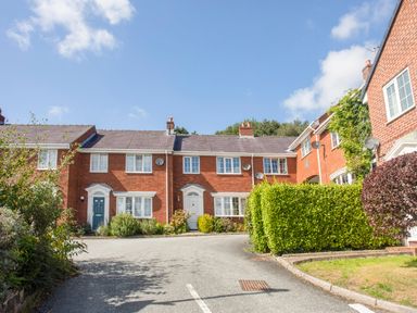 A driveway leading to red brick townhouses with white doors and windows surrounded by green hedges at Sea View Cottage in Menai Bridge