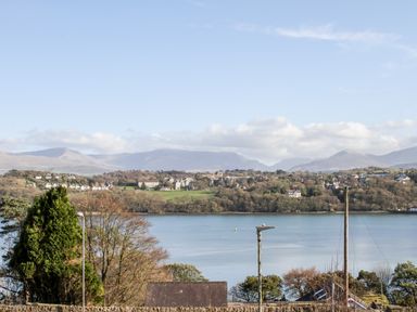 A view of a body of water with houses and trees on the opposite shore and mountains in the background at Sea View Cottage Menai Bridge