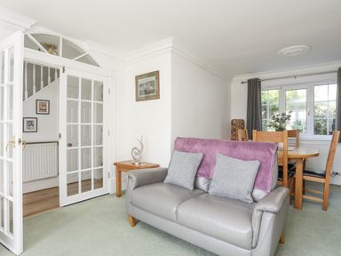 A living room with a grey leather sofa and purple throw next to a wooden dining table and chairs at Sea View Cottage in Menai Bridge