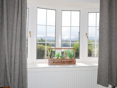 A window with white frames and gray curtains with a wooden planter box holding small plants on the windowsill at Sea View Cottage in Menai Bridge