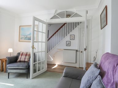 A living room with armchairs pillows and a wooden side table by an open glass door showing a staircase at Sea View Cottage in Menai Bridge