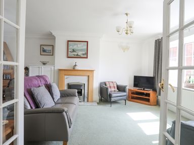 A living room with a sofa an armchair a TV on a wooden stand a fireplace and paintings on the walls at Sea View Cottage in Menai Bridge