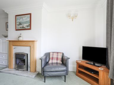 A living room with a fireplace armchair with cushion and television on stand at Sea View Cottage in Menai Bridge