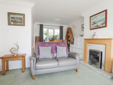 A living room with a gray leather sofa and two pillows a wooden fireplace and framed paintings at Sea View Cottage in Menai Bridge