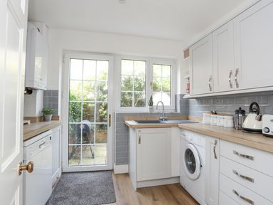 A kitchen with white cabinets a washing machine a dishwasher a sink and a glass door leading outside at Sea View Cottage in Menai Bridge