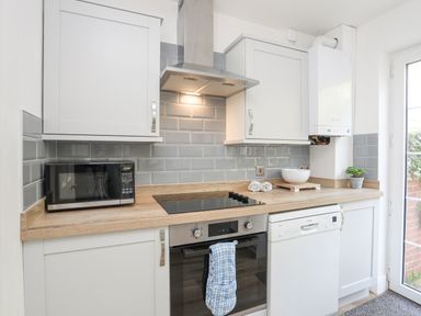 A kitchen countertop with a microwave oven stovetop oven dishwasher and white cabinets at Sea View Cottage in Menai Bridge