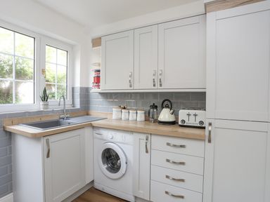 A kitchen with a sink under a window washing machine toaster and kettle at Sea View Cottage in Menai Bridge