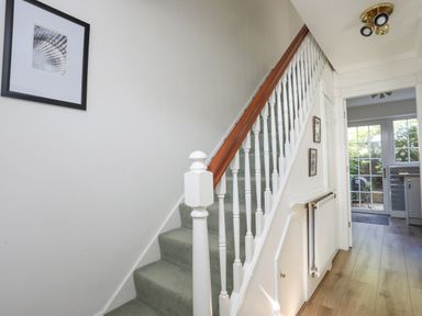 A hallway with carpeted stairs and wooden handrail leading to an upper floor and a door opening to a room with glass doors at Sea View Cottage in Menai Bridge