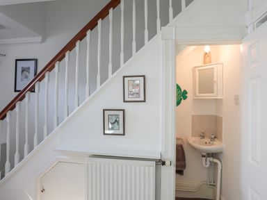 A stairway with white spindles and a wooden handrail next to a small bathroom with a sink and mirror at Sea View Cottage in Menai Bridge