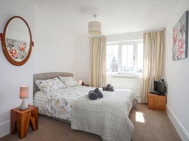 A bedroom with a bed with floral bedding two wooden nightstands lamps a wall mirror a window with curtains and a small TV on a wooden stand at Sea View Cottage in Menai Bridge