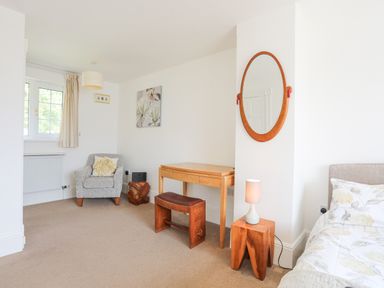 A bedroom with a wooden dressing table and bench a wooden side table with a lamp an armchair and a bed at Sea View Cottage in Menai Bridge