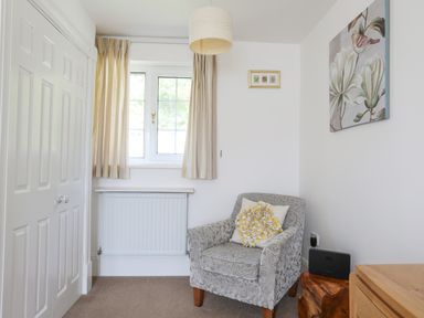 A small room with a patterned armchair and cushion a wooden side table a window with curtains and white closet doors at Sea View Cottage in Menai Bridge
