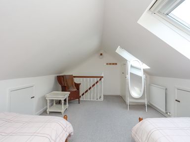 An attic bedroom with two beds a wicker chair a small table a standing mirror radiator and skylight windows at Sea View Cottage in Menai Bridge