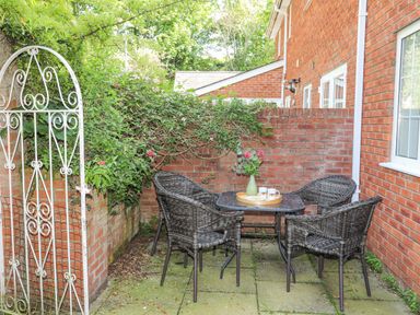 An outdoor patio with a metal table, four wicker chairs, a tray with cups and flowers, and a white metal gate at Sea View Cottage in Menai Bridge