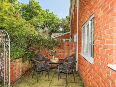 A small outdoor patio with a table and four wicker chairs next to a brick wall at Sea View Cottage in Menai Bridge