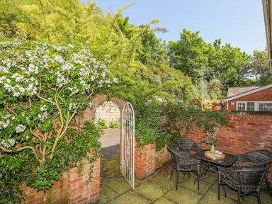 A brick patio with a metal gate wicker chairs and a table with flowers on the table at Sea View Cottage in Menai Bridge