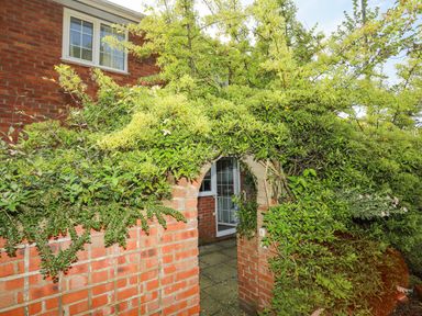 A brick archway covered in green vines leading to a patio outside a red brick house at Sea View Cottage in Menai Bridge