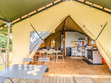 An open tent with a kitchen area dining table wooden chairs and an outdoor table with jars and a domino game at Honey @ Stars & Embers Glamping in Grampound