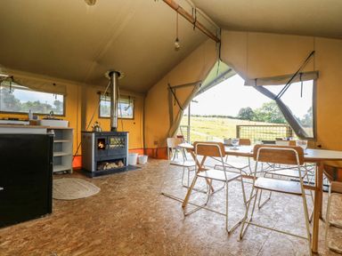 An interior view of a tent with a wood stove dining table with chairs and a small kitchen area at Honey @ Stars & Embers Glamping Grampound