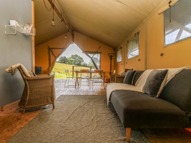 A glamping tent interior with a sofa and armchairs and a dining table with chairs at Honey @ Stars & Embers Glamping in Grampound