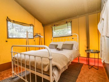 A bedroom with a metal bed frame a blanket a bedside table with a tray and a clothing rack at Honey @ Stars & Embers Glamping in Grampound