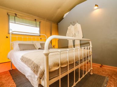 A bedroom with a white metal bed frame two pillows two bathrobes hanging on the wall and a wall light at Honey @ Stars & Embers Glamping in Grampound