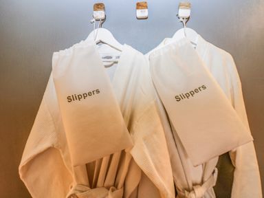 Two white bathrobes hanging on hooks with slippers bags attached at Honey @ Stars & Embers Glamping in Grampound
