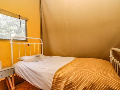 A bed with white metal frame and yellow blanket beside a window and small table at Honey @ Stars & Embers Glamping in Grampound