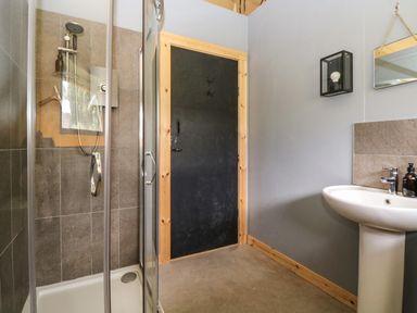 A bathroom with a glass shower enclosure a black door a white pedestal sink and a wall-mounted mirror at Honey @ Stars & Embers Glamping in Grampound