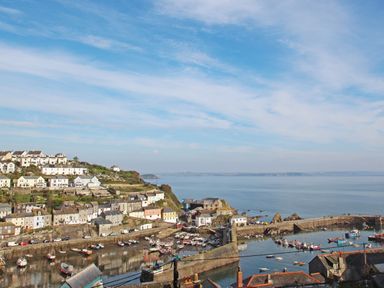 A coastal village with houses on a hillside overlooking a harbor filled with boats and a sea in the background at Honey @ Stars & Embers Glamping in Grampound