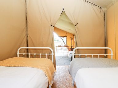 A tent interior with two beds and a view of a dining area with chairs and a coat rack at Bumble @ Stars & Embers Glamping in Grampound