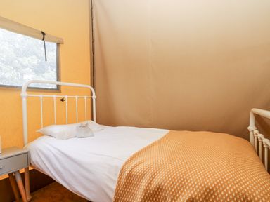 A bed with white sheets and an orange blanket next to a small grey nightstand under a window in a tent at Bumble @ Stars & Embers Glamping Grampound
