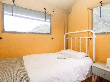 A bedroom with a white metal bed frame a bedside table and two windows at Bumble @ Stars & Embers Glamping in Grampound