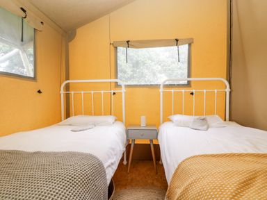 A bedroom with two single beds with white metal frames and blankets with a small bedside table in the middle at Bumble @ Stars & Embers Glamping Grampound