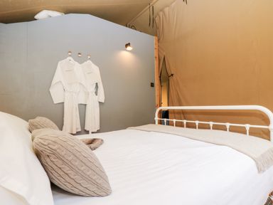 A bedroom with a white metal bed frame two beige pillows and two white bathrobes hanging on a wall at Bumble @ Stars & Embers Glamping in Grampound