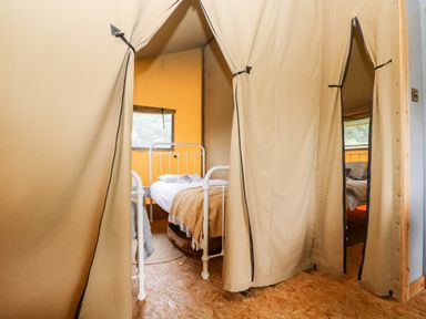 A tent interior with two single metal frame beds and beige curtains at Bumble @ Stars & Embers Glamping in Grampound