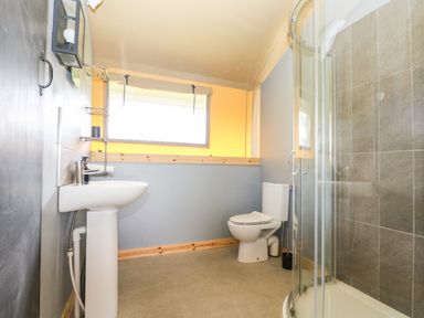 A bathroom with a pedestal sink toilet and a curved glass shower enclosure at Bumble @ Stars & Embers Glamping in Grampound